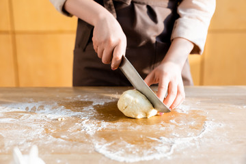 cropped view of young woman cutting dough on wooden table