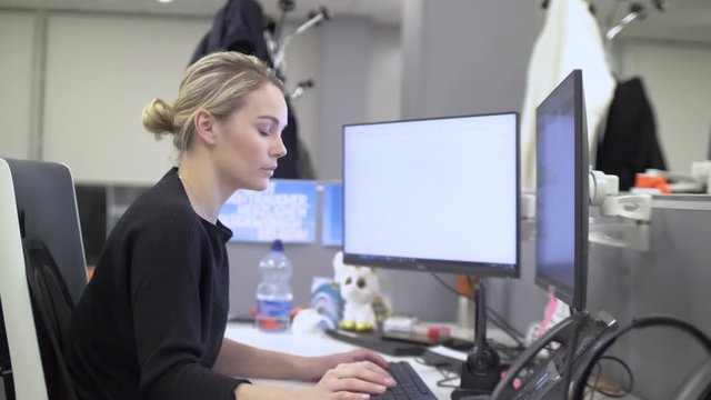Blonde female employee is working on a computer with two screens. Slow Motion