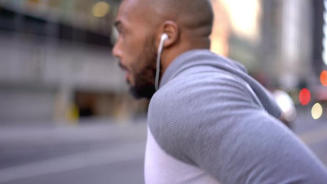 Strong african american male runner in trendy sportswear jogging in morning on urban setting in downtown listening playlist in earphones