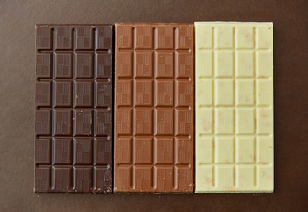 sweets, confectionery and food concept - milk, dark and white chocolate bars on brown background