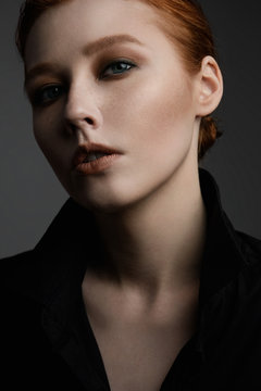 Close portrait of a red-haired girl with freckles and blue eyes, with perfect skin in a black shirt.
