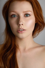 Fototapeta premium A close portrait of a red-haired girl with freckles and blue eyes, with radiant skin and loose hair on her bare shoulders.