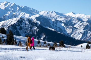 Man and woman are hiking in snow mountains with dog. Trekking in mountains in winter.