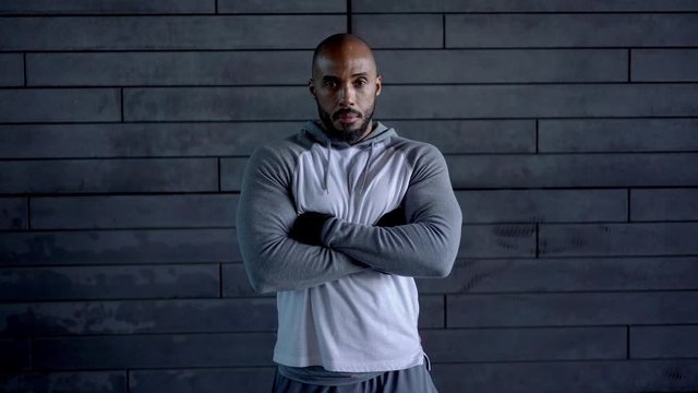 Young african american male athlete in trendy active outfit standing on copy space wall with hands crossed smiling and looking at camera 