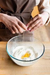 cropped view of woman adding raw egg in bowl with flour