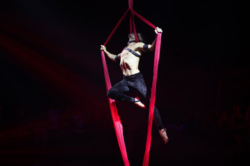 Brazilian strong sexy man do performance on aerial silks in red lights.  Sport training gym and lifestyle concept.