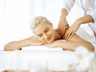 Fototapeta na wymiar Beautiful blonde woman enjoying back massage with closed eyes. Spa salon concept