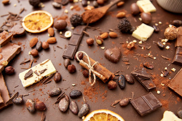 sweets, confectionery and culinary concept - cocoa beans, chocolate, nuts and cinnamon sticks on brown background
