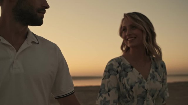 A young couple in love are having a date while walking and holding hands together on the beach near the lake