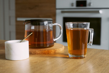 Glass cup and teapot with tea in the kitchen