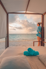 Tanned girl in shorts on sea beach blue beach dress. Tanned blonde woman in tropical beach scene, close to sea posing on the evening sea beach under a wooden canopy. Carefree vacation concept