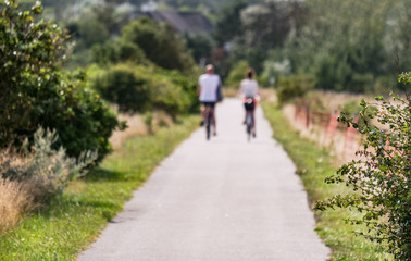 Kein Fokus, bewusst unscharf: Junges Paar fährt im Sommer mit Fahrrädern durch eine nordische...