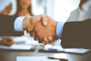 Business people shaking hands at meeting while theirs colleagues clapping and applauding. Group of unknown businessmen and women in modern white office. Success teamwork, partnership and handshake