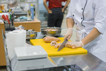 Chef carves whole raw chicken carcass with knife on yellow plastic board at cuisine of restaurant....