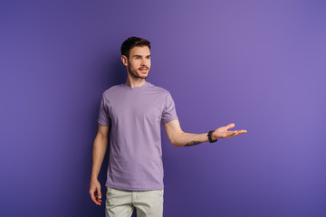 positive handsome man standing with open arm while looking away on purple background