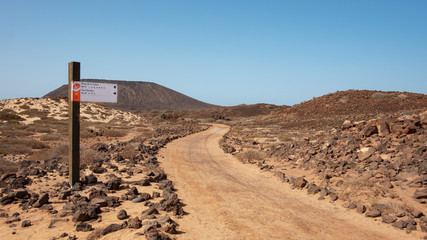 Walking or hiking marker showing the distances to the beach and lighthouse on the side of an empty path through the rough land, Los Lobos,  Fuerteventura, Canary Islands, Spain