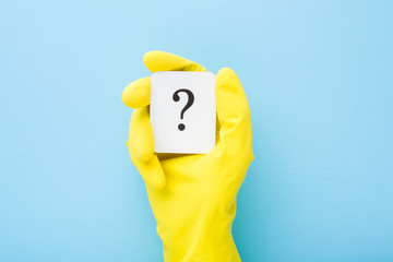 Cleaner hand in yellow rubber protective glove showing white card of question mark on light blue...