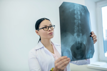 Dark-haired female doctor analyzing xray results of backbones