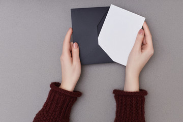 Woman's hands holding an empty postcard and black envelope on the grey background. Christmas concept