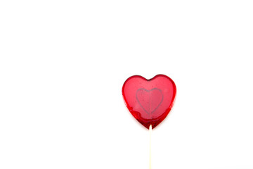 Sweet lollipop in the form of a heart of red-transparent color on a wooden stick on a white isolated background. Love and feelings in candy.