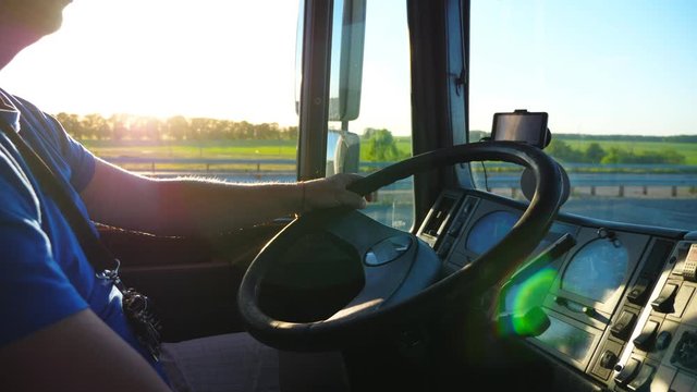 Unrecognizable man sitting behind wheel of his truck and riding through countryside at sunset. Close up steering wheel and dashboard of truck. Beautiful landscape at background. Slow motion Side view