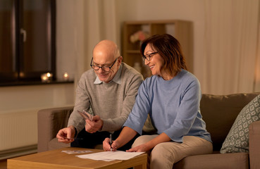 family, savings and people concept - smiling senior couple with bills counting money at home
