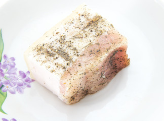 Slice of freshly salted pork fat sprinkled with pepper on a ceramic plate with a pattern (flower). Lard with meat and skin. Traditional food of Russia and Ukraine.