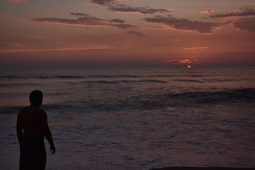 a man standing in a beach to see the sun set in the middle of a ocean