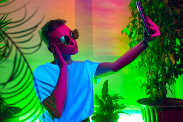 Style. Cinematic portrait of stylish woman in neon lighted interior. Toned like cinema effects, bright neoned colors. Caucasian model using smartphone in colorful lights indoors. Youth culture.