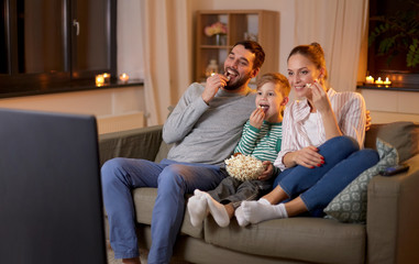 family, leisure and people concept - happy smiling father, mother and little son watching tv and...