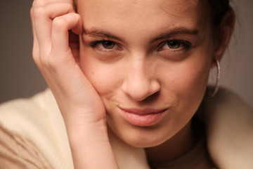 A close-up portrait of a beautiful young girl with brown hair and green eyes with natural makeup in light clothing