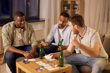 leisure games, friendship and gambling - male friends playing cards and drinking beer at home at night