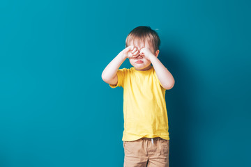 Upset crying sad boy at blue background, looking at camera.