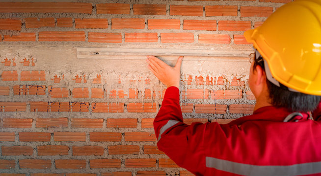 Plasterer in red working uniform plastering the wall indoors.