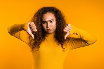 Young pretty woman standing on yellow studio background expressing discontent and showing thumb...