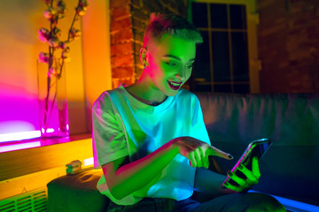 Happy. Cinematic portrait of stylish woman in neon lighted interior. Toned like cinema effects, bright neoned colors. Caucasian model using smartphone in colorful lights indoors. Youth culture.