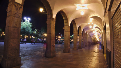 Night photograph of stone portals with arches and groves on one of the side faces of the main square of the city of Arequipa in Peru.