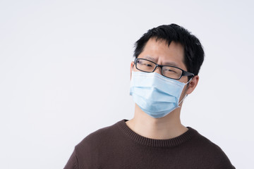Young Asian man portrait, feeling sick, wearing a surgical blue face mask to prevent infection, air pollution isolated on white background, cut out.