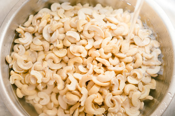 Closeup, Pouring water to soak and wash cashew nuts in bowl to remove dirts, tannins, phytic acid. Healthy & high nutrient food, good for digestion of plant based diet, vegan, vegetarian & keto.