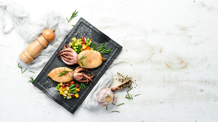 Baked squid with vegetables in a black stone plate. Seafood. Top view. Free space for your text.