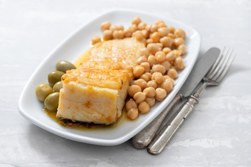 fried cod fish with chick pea and olives on white dish on ceramic background