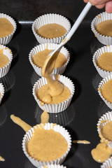 Top view of person placing dough for muffins in paper molds, in cooking class, on baking sheet, in vertical