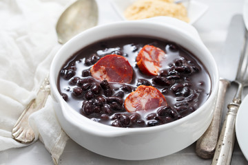 typical brazilian food black beans with smoked sausages in white bowl