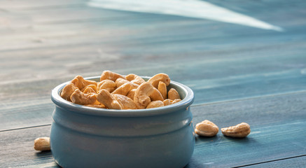 Cashew nuts in a blue cup on a blue wooden table.