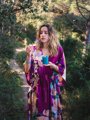 Very pretty young woman with a candle and a hand-painted silk dress in the forest doing a meditation ritual