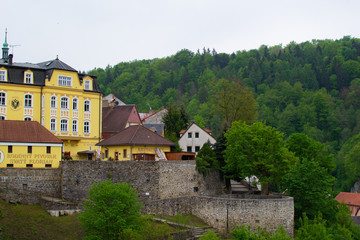 Fototapeta na wymiar Loket, Czech Republic; 5/20/2019: Yellow building of St. Florian Brewery restaurant, with the stone wall at the foreground and trees at the background