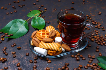 Black tea in glass cup with sweets on dark background
