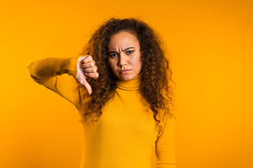 Young pretty woman standing on yellow studio background expressing discontent and showing thumb...