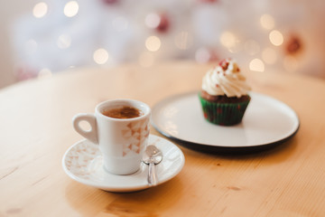 Italian coffee Cup and cupcake on the table near the Christmas tree with white bokeh