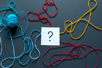 Question mark drawn on notes and a ball of thread on the dark background.
